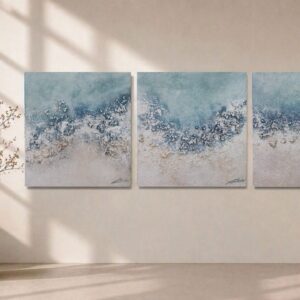 Tríptico de cuadros abstractos de playas mediterráneas con relieve y texturas de olas marinas colgados en un salón de diseño minimalista.